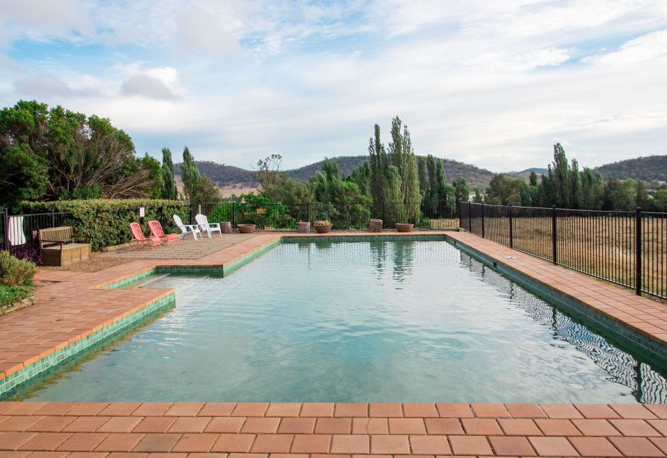 a large swimming pool with a brick deck and lounge chairs is surrounded by trees at Stay in Mudgee
