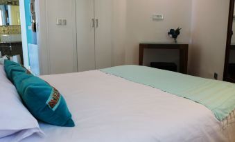 a neatly made bed with a blue pillow and white sheets , located in a room with white walls and cabinets at The View Gammarth