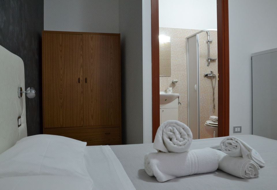 a white bed with rolled up towels on it , next to a bathroom with a shower at B&B Il Molo