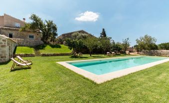 a large swimming pool is surrounded by a grassy area and trees , with a mountain in the background at Baglio Occhipinti