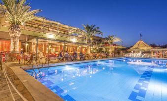 a large swimming pool is surrounded by palm trees and chairs , with a building in the background at Golden Sand Hotel