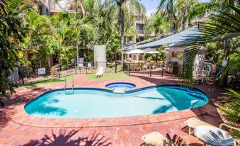 a large swimming pool is surrounded by a wooden deck , umbrellas , and lounge chairs in a tropical setting at Sanctuary Beach Resort