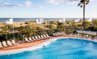 a large outdoor swimming pool surrounded by lounge chairs and umbrellas , with a view of the ocean in the background at DoubleTree by Hilton Islantilla Beach Golf Resort