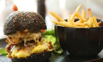 a hamburger with a side of french fries and a bowl of salad on a table at Yats Colony