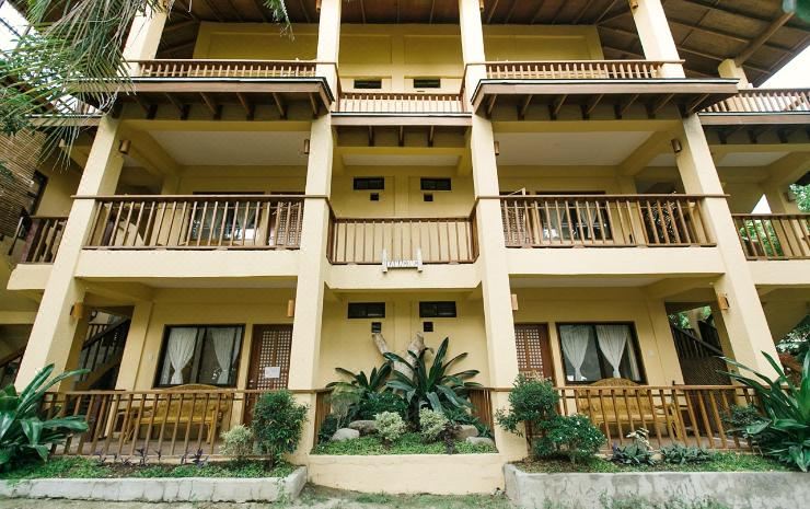 a multi - story building with wooden balconies and stone flooring , surrounded by greenery and potted plants at La Luz Beach Resort