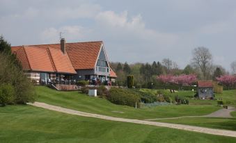 a large building with a red roof is situated on a golf course , surrounded by green grass and trees at Hôtel du Golf