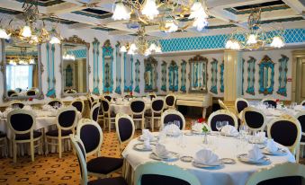 a large dining room with white tables and chairs , blue and white walls , and chandeliers hanging from the ceiling at Hotel Roman by Dumbrava Business Resort