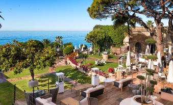 a large outdoor patio with a view of the ocean and trees , featuring several chairs and tables at El Fuerte Marbella