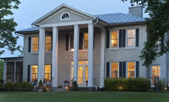 a large stone house with columns and a gray roof , situated in a grassy field at Steeles Tavern Manor