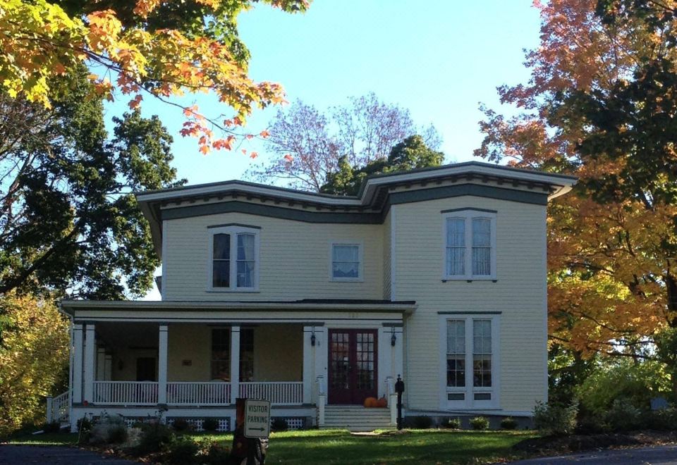 a large white house with a porch and two dogs in front of it , surrounded by trees at Finger Lakes Bed and Breakfast