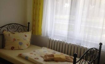 a bed with a yellow blanket and black metal frame is placed near a window with white curtains at Weißes Haus