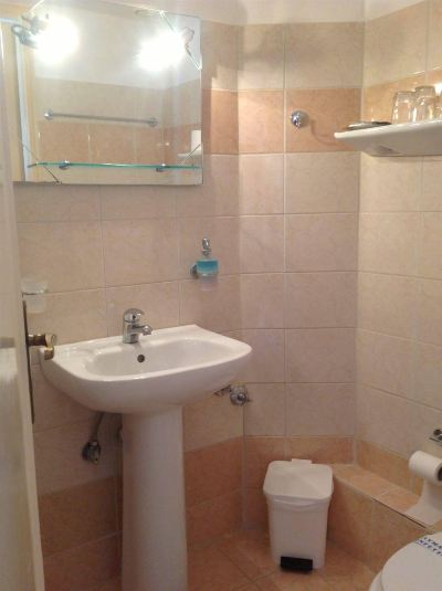 a modern bathroom with beige tiles , white walls , and a glass shelf above the sink at Hotel Summery