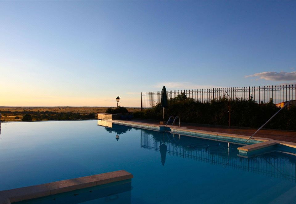 a large outdoor swimming pool surrounded by a fence , with the sun setting in the background at Hotel El Rancho