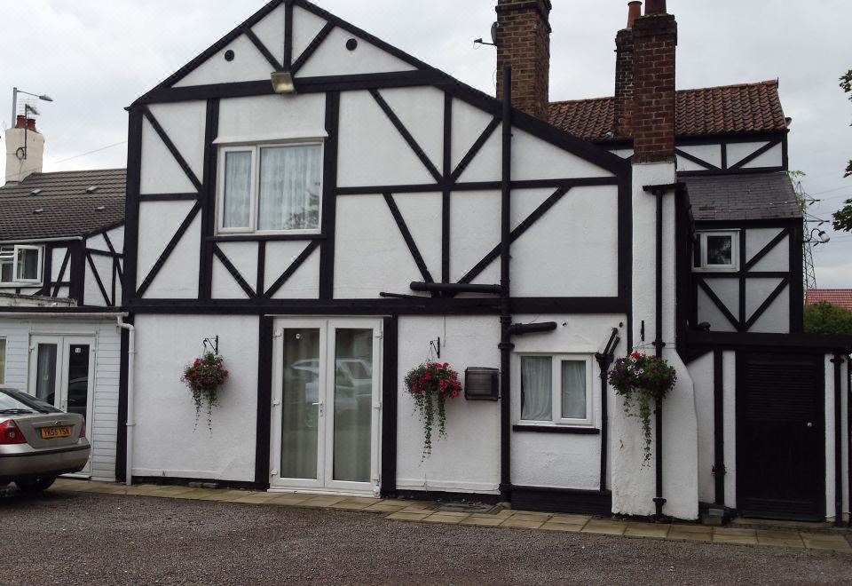 a white and black two - story house with a black roof , situated on a street corner at Tudor House