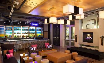 a modern lounge area with couches , chairs , and tables in front of a large screen at Aloft Chesapeake