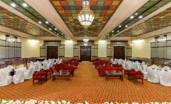 a large , empty conference room with red and white chairs and a colorful ceiling , set up for a formal event at Faisalabad Serena Hotel