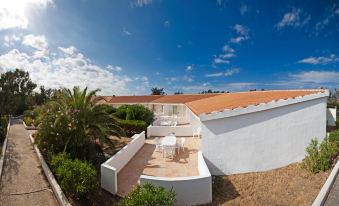 a white building with an orange roof , surrounded by palm trees and other greenery , under a clear blue sky at La Plage Resort