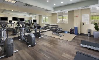 a well - equipped gym with various exercise equipment , including treadmills and weightlifting machines , under bright lights at Holiday Inn & Suites Arden - Asheville Airport