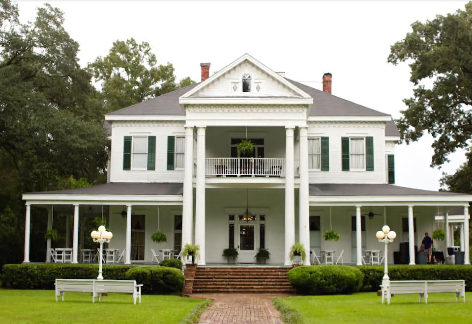 a large white house with a porch and benches in front of it , surrounded by green grass at Blythewood Plantation