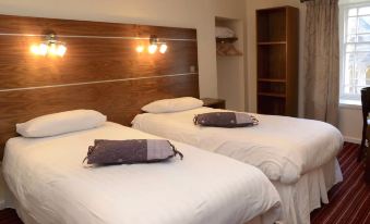 a hotel room with two beds , each made up with white sheets and pillows , next to a wooden headboard at County Hotel