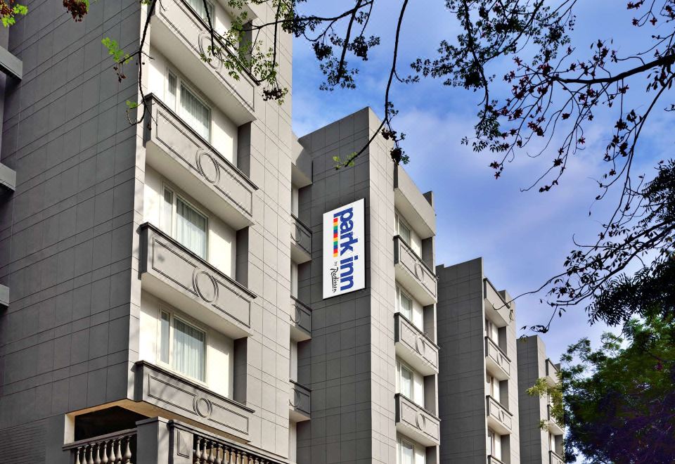 a tall apartment building with multiple balconies and a blue sign on the side , set against a clear sky at Park Inn by Radisson New Delhi Lajpat Nagar