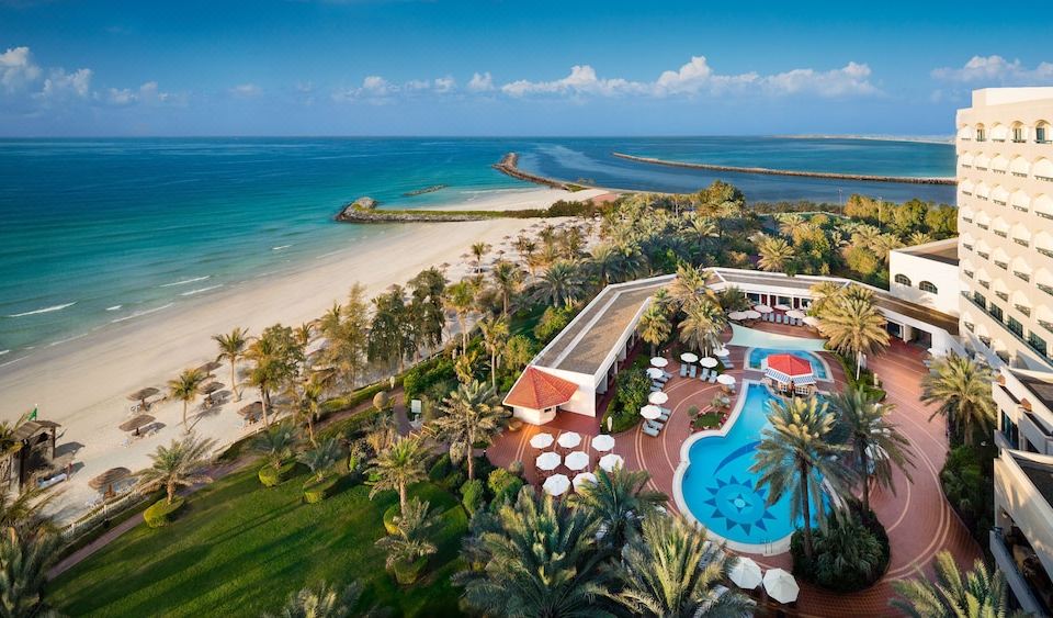 aerial view of a beach resort with a pool , palm trees , and a sandy shoreline at Ajman Hotel by Blazon Hotels