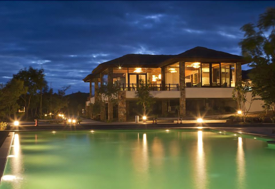 a large house with a pool in front of it , surrounded by trees and lit up at night at The Serai Bandipur