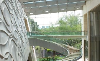 a modern building with a curved glass wall , surrounded by lush greenery and a winding staircase leading to an upper level at Hilton Bandung