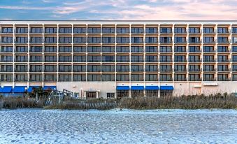 a large hotel building surrounded by snow - covered grass and a body of water , possibly a lake or pond at Crystal Coast Oceanfront Hotel