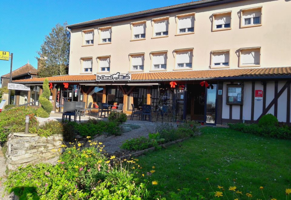 a large building with a restaurant on the ground floor and a restaurant on the ground floor , surrounded by greenery at Le Cheval Blanc - Logis Hotel