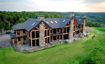 a large wooden house with stone accents and a green lawn , surrounded by trees and mountains at Mont du Lac Resort