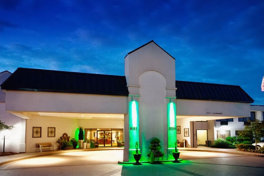 a large building with a green and white facade , lit up at night , and a fountain in front of it at Best Western Plus Madison-Huntsville Hotel