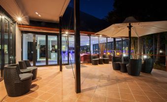 an outdoor patio area with a dining table , chairs , and umbrellas under a large glass window at Springwood Motor Inn