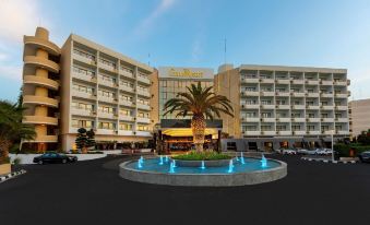 a large hotel building with a fountain in front of it , surrounded by a parking lot at The GrandResort - Limited Edition by Leonardo Hotels