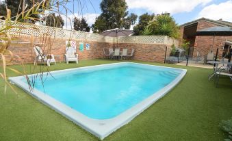 a backyard with a green lawn , a pool , and a patio area surrounded by chairs and a table at Sandhurst Motor Inn Bendigo