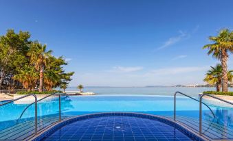 a large swimming pool with a blue tiled edge is surrounded by palm trees and overlooks the ocean at Le Méridien Lav, Split