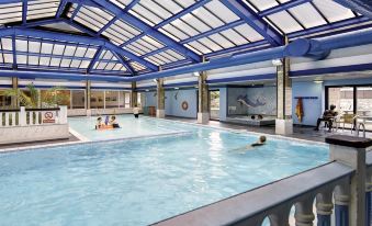 a large swimming pool with a glass ceiling and people in the water below at Best Western Weymouth Hotel Rembrandt