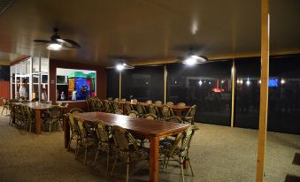 a large room with several long wooden tables and chairs , a projection screen on the wall , and windows at Peppermill Inn Motel