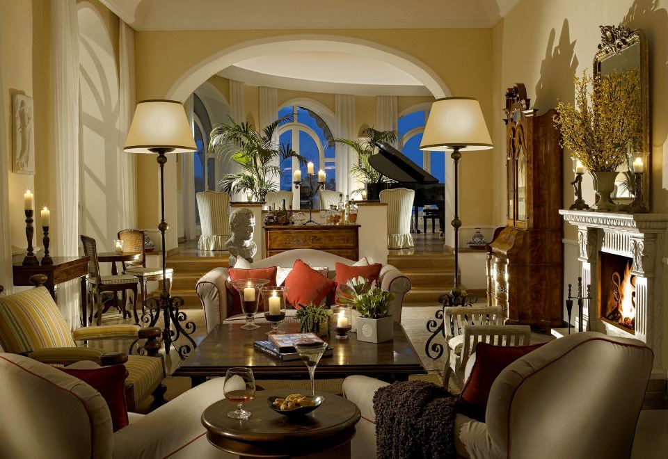 a spacious living room with high ceilings , white walls , and various furniture pieces including sofas , chairs , and potted plants at Hotel Caesar Augustus