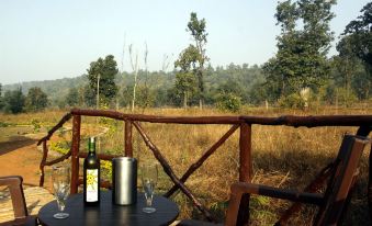 a wooden balcony overlooking a lush green field , with two wine bottles and glasses placed on the table at Wildflower Resort