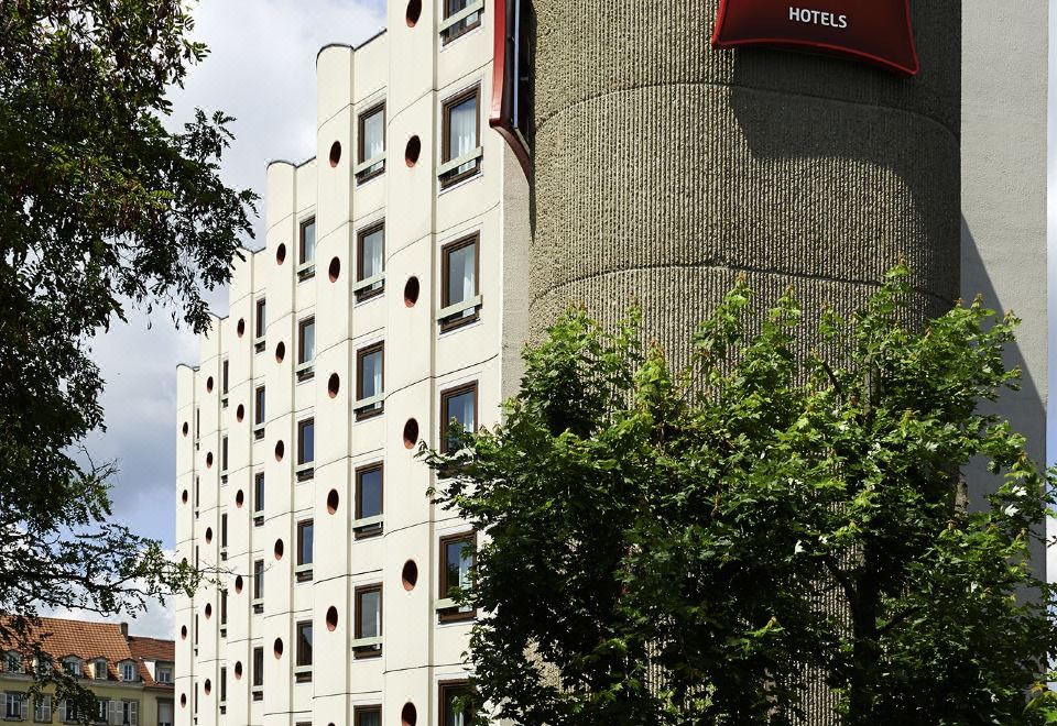 a tall hotel building with a red banner on top , located in a city setting at Ibis Strasbourg Centre Historique