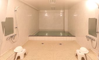 a white bathtub with a shower and two white plastic stools in a room with tiled walls at Sakuraya