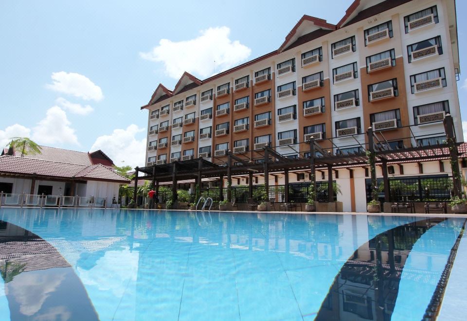 an outdoor swimming pool surrounded by a hotel , with several people enjoying their time in the pool at Permai Hotel Kuala Terengganu