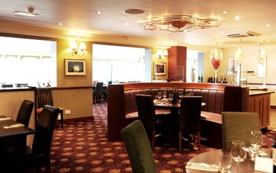 a dining room with a large dining table surrounded by chairs , and a wine cellar in the background at Village Hotel Liverpool