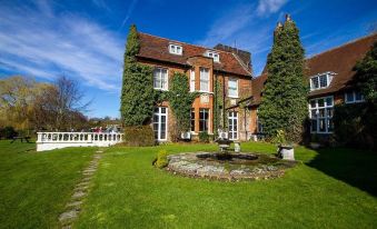 a large , orange - roofed building with green trim , surrounded by lush greenery and a small fountain in the yard at Letchworth Hall