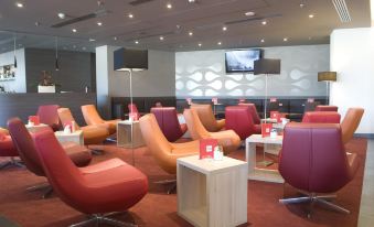 a modern lounge area with colorful chairs and tables , a television on the wall , and purple cushions at Park Inn by Radisson Krakow