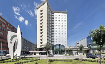 a tall white building with many windows is surrounded by green grass and trees , with a few smaller buildings in the background at Hotel Continental