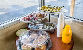 a dining table with a variety of food items , including sandwiches , fruits , and drinks , placed on a wooden surface near a window at Economy Inn & Suites