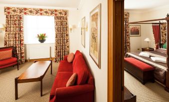 a red couch is in a room with two windows and a wooden table at Mercure York Fairfield Manor Hotel
