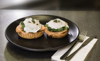 two slices of bread topped with eggs and greens , placed on a black plate , accompanied by a fork and knife at Athelstane House